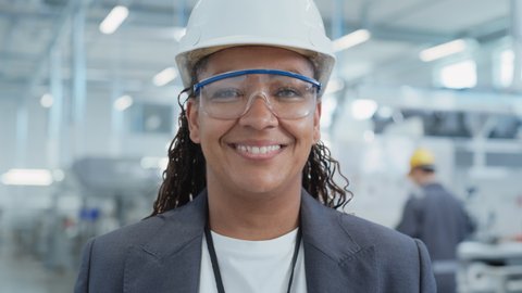 Close Up Portrait of a Successful, Happy and Smiling African Female Engineer in White Hard Hat Standing at Electronics Manufacturing Factory. Black Heavy Industry Specialist Posing for Camera.