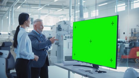Factory Office Meeting: Chief Engineer Talking with Business Partner in a Conference Room with TV with Green Screen Mock Up Display. Concept for Heavy Industry and Manufacturing Related Templates.