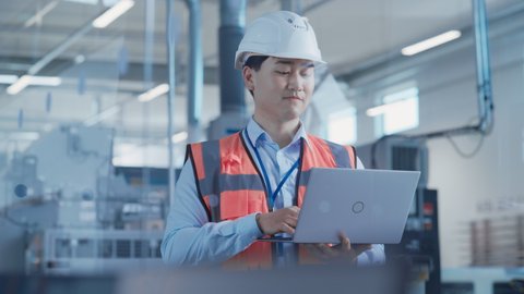 Research and Development Specialist Using Laptop to Operate a Heavy Industry Machine at a Factory. Asian Male Technician Configuring Industrial Machinery with the Help of Computer.