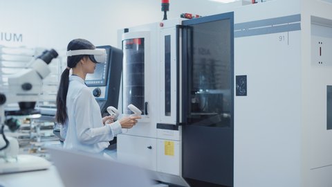 Professional Research and Development Specialist Wearing a Virtual Reality Headset and Operating a Heavy Industry Machine at a Factory. Technician Configuring Industrial Machinery with VR Technology.