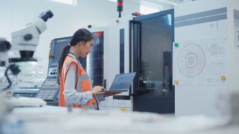 Research and Development Specialist Using Laptop to Operate a Heavy Industry Machine at a Factory. Asian Female Technician Configuring Industrial Machinery with the Help of Computer.