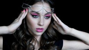 Beauty closeup slow motion video of young woman with hand near face. Brunette girl with an oriental appearance with pink makeup and rhinestone embellishment on the head.