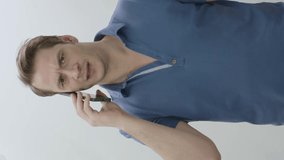 Worried offended and angry young man standing talking on the phone.Angry young man talking on mobile phone isolated on white background.Tense,crazy professional talk on smartphone.Vertical video.