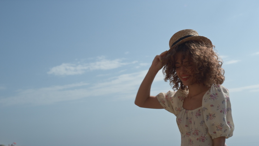 Cheerful cute girl frolicing jumping on seashore summer day close up. Happy carefree woman holding straw hat on bouncing curls. Attractive smiling lady dancing in ocean water enjoy serene vacation. Royalty-Free Stock Footage #1092386395