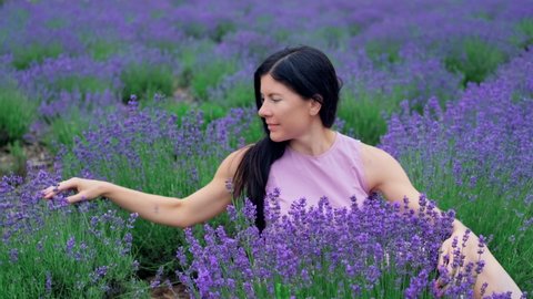 Young woman enjoying lavender aromatic flowers. Female gently touching blooming lavender. Violet fragrant lavender flowers on field. 4K, UHD