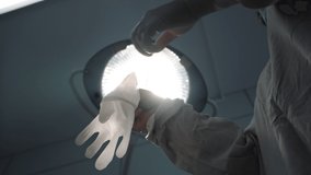 Slow motion, surgeon doctor in medical protective suit preparing for surgery, healthcare worker putting on white rubber latex gloves backlit by surgical shadowless lamp light, hospital operating room. - Powered by Shutterstock - Get 15% off with code: PIKWIZARD15