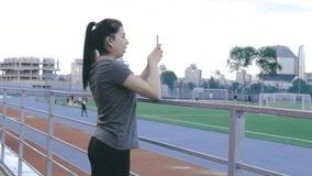 Young pretty female taking video of football players playing football on the field at stadium. College student sportwoman doing live stream for sport supporters spectators