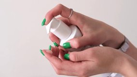 Women's hands with green manicure squeeze the cream out of the bottle using a dispenser. Slow motion video