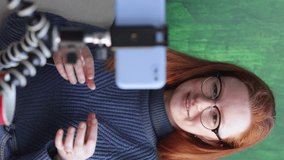woman speaks via video link with colleagues or conducts a training webinar. red-haired European woman takes notes in a notebook and communicates via video chat from a smartphone. a female blogger or a