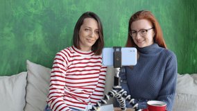 two female bloggers or students watch a training webinar online from a smartphone, conduct a live broadcast for subscribers. beautiful successful European women in coworking watch online training and