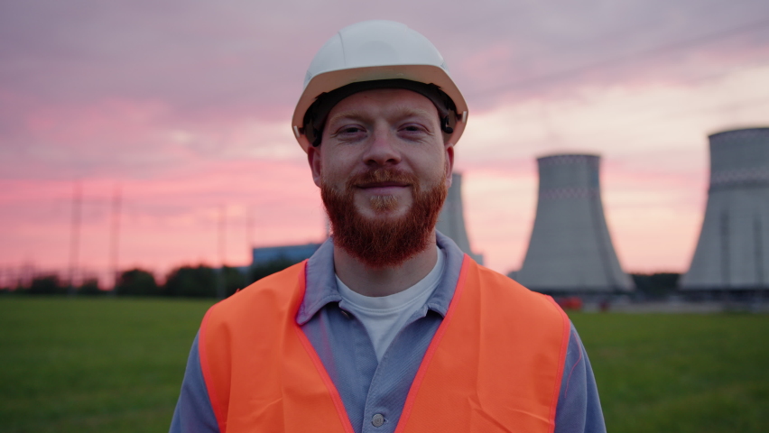 Portrait of a male engineer in a helmet and vest who looks into the camera with a smile