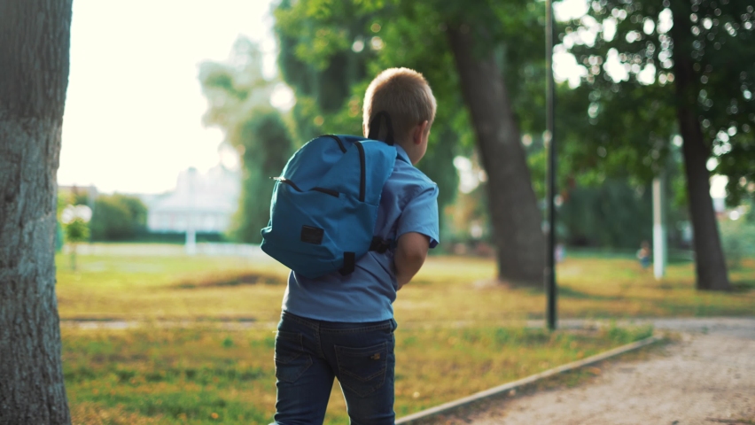 Happy boy with backpack goes to school. Child goes back to school. Kid walks along path in the park. Schoolboy with backpack goes to school. Children's education concept. Child goes to first grade Royalty-Free Stock Footage #1092417689
