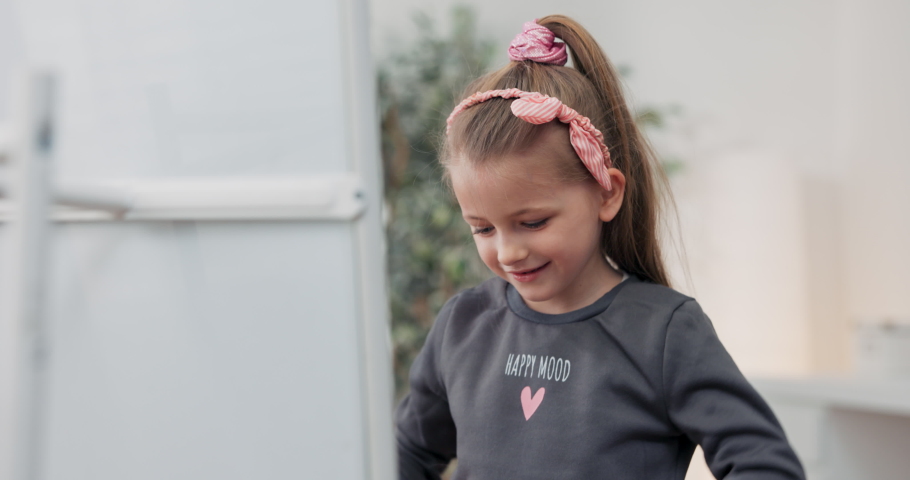 Little girl choosing clothes in front of the mirror. Child thinks what to choose to wear large selection of dresses on hangers. Concept of selling, buying.