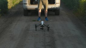 Horizontal view of unrecognized young man standing near car and launching drone. Footage of male drone operator using quadcopter. Smart technologies. Farmland, out of town. Outdoor, summertime