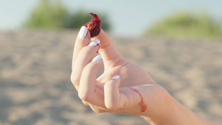 A girl on the beach holds a bitten cherry berry, red juice flows down her arm, close-up.