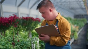Happy young employee with Down syndrome working in garden centre, taking care of flowers. - Powered by Shutterstock - Get 15% off with code: PIKWIZARD15