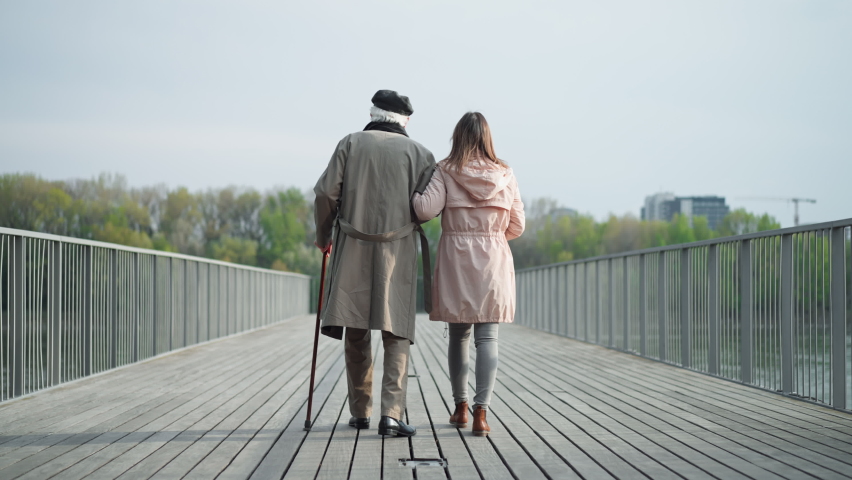 Rear view of senior man with daughter outdoors on a walk on pier by river. Royalty-Free Stock Footage #1092421375