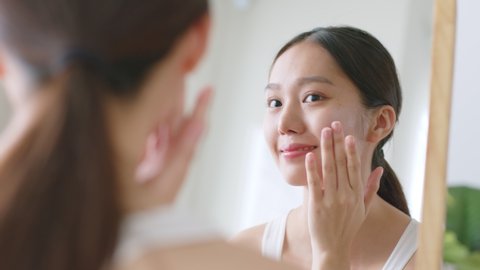 Young Asian woman apply serum and moisturizing cream on healthy facial beauty skin and look at mirror วิดีโอสต็อก