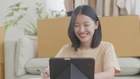 Asian young woman presenting through Livestream selling clothes online with fun and happiness. Young woman sitting on the floor using a smartphone to live stream at home on vacation