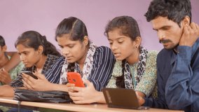 Group of teenager students busy using mobile phone while sitting on classroom - concept of technology, social media addiction and friendship.