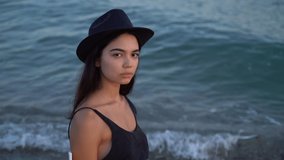 young brunette beautiful woman in hat in profile in front of sea. Romantic Slow motion video footage. disturbing anxious haughty eyes look movement of the waves on the background. 