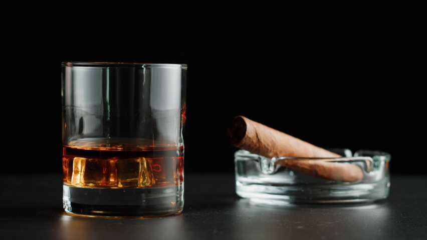 Brandy or whiskey and cigar close-up. Luxury cognac with ice on black background. Alcohol amber drink, drinking rum, liqour beverage in glass. | Shutterstock HD Video #1092432659