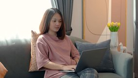 4K, Medium shot Asian woman sitting in front of her laptop talking on video call in online learning at home. sitting on the sofa in the living room of the house using a laptop computer
