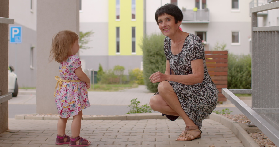 Grandmother and granddaughter in courtyard house. She keeps her back straight, posing, looking camera girl stands, turns her head. Meeting close people. distance in communication.