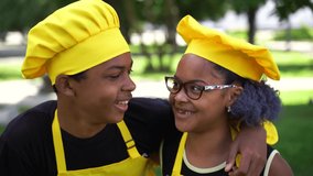 4k video African cooks children grimacing and smiling in yellow chefs hat and apron. Black African brother and sister cooking and having fun together.
