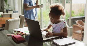 Vertical video of african american father and daughter using laptop and learn. Enjoying quality family time together at home, using technology.