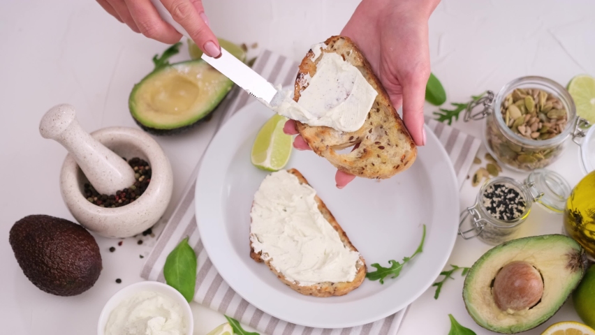woman standing at kitchen spreading whizzed cream cheese on slice of bread with butter knife