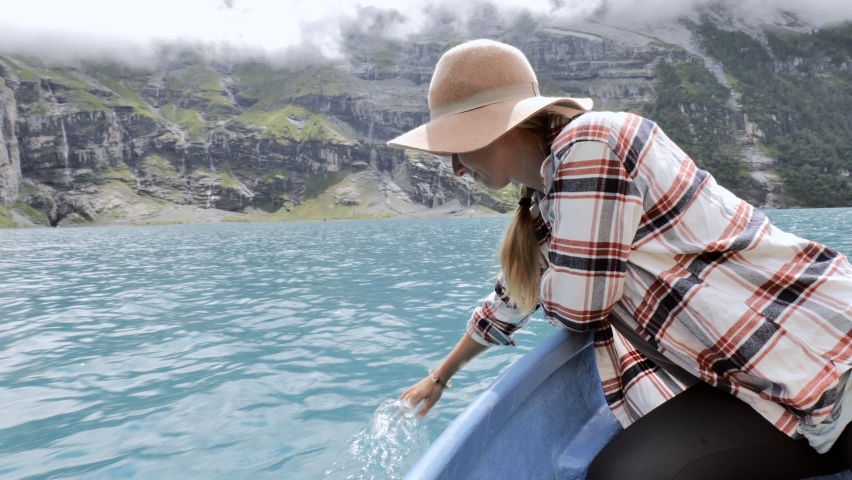 Cheerful young woman touches the surface of an alpine lake from a rowboat 