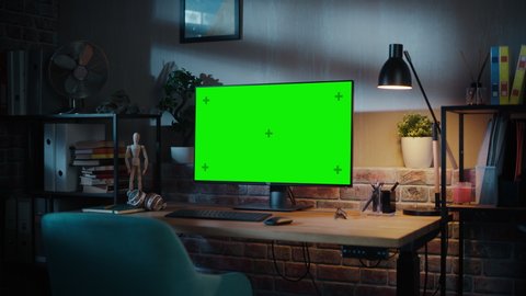Computer Monitor with Green Screen Standing on a Wooden Desk with Height Adjustable Function. Chroma Key Display at Home in Modern Living Room or Creative Loft Office with Brick Wall. Zoom In Shot.