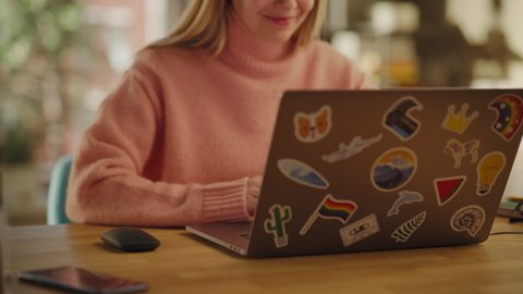 Close Up of a Beautiful Young Adult Woman Using Laptop Computer with LGBT Stickers on the Back in Creative Loft Office Space. Happy Specialist in Warm Cozy Sweater Working from Home.