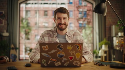 Stylish Bearded Young Adult Man Using Laptop Computer with LGBT Stickers on the Back in Creative Loft Office Space. Happy Specialist in Checkered Shirt Looking at Camera, Smiling.