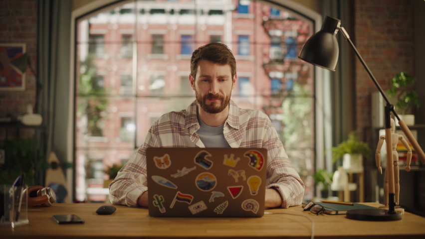Professional Creative Man Sitting at a Desk at Home Office Studio, Working on Laptop Computer. Specialist Thinking About a Good Email Reply. Great Idea Comes and He Types It Down. Zoom In Shot.