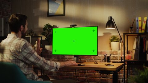 Office Employee Working from Home, Talking on Video Call on Desktop Computer with Monitor with Green Screen Mock Up. Man Sitting in Living Room, Chatting Online with Friends and Family in the Evening.