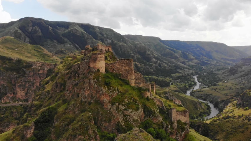Aerial panning view dramatic landscape with historical Tmogvi fortress ruins with old wall on hilltop surrounded scenic Mtkvari river and canyon panorama