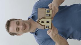 Analyze to buy or invest in a house or real estate.Happy young man examining blueprint model of new house he bought or rented isolated on white background.New construction project.Vertical video.