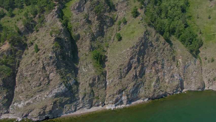 Aerial video footage of a rocky shore overgrown with forest and grass. Wildlife. Natural reserve. Top view. 
