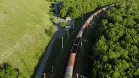 Aerial view on railway freight cars train moving on the rail road curve among green hills and forest green trees. Rail way freight cargo train