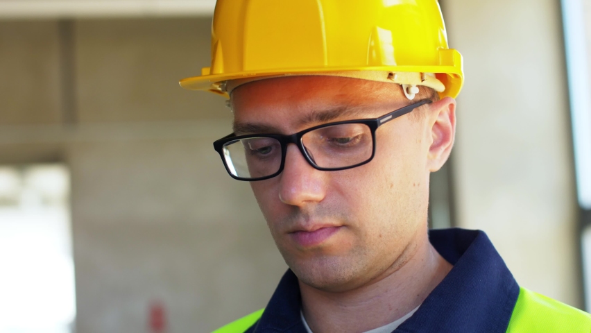 construction business and building concept - male builder in helmet and safety west with smartphone