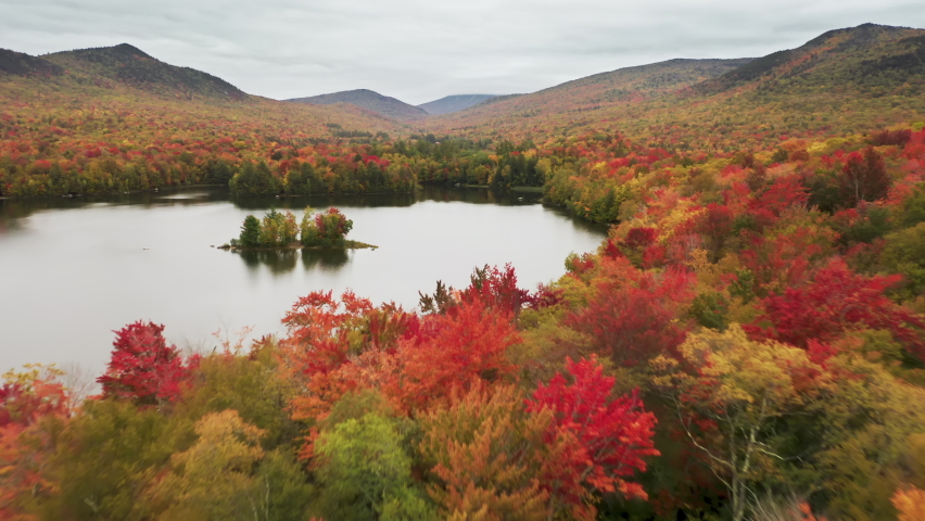 Beautiful fall nature landscape with woodland hills on cloudy autumn day background. Aerial view of scenic small island with trees in the middle of the cinematic lake with scenic still water surface