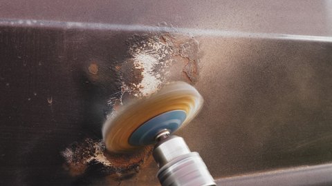 A round metal brush, automatic in the hands of a craftsman, removes rust and paint from a car door. Medium plan