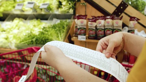 Woman checks paper check after shopping for groceries at mall by checking Dear Amount bill in a grocery cart. increase in food prices, spending money in hypermarket. Woman checking grocery store cart 스톡 비디오
