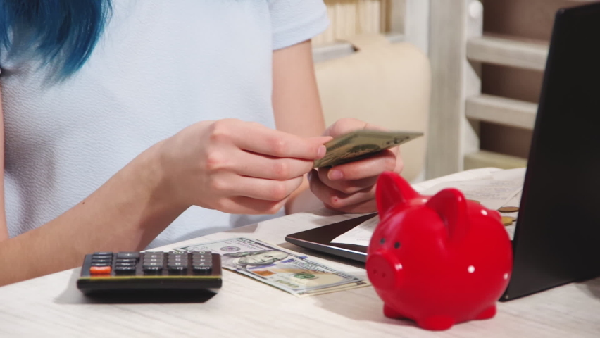 Women's hands count US dollars on a table next to a laptop, a piggy bank and a calculator. Tuition fees. Payment of taxes. Online shopping. The concept of saving money for financial accounting | Shutterstock HD Video #1092472961