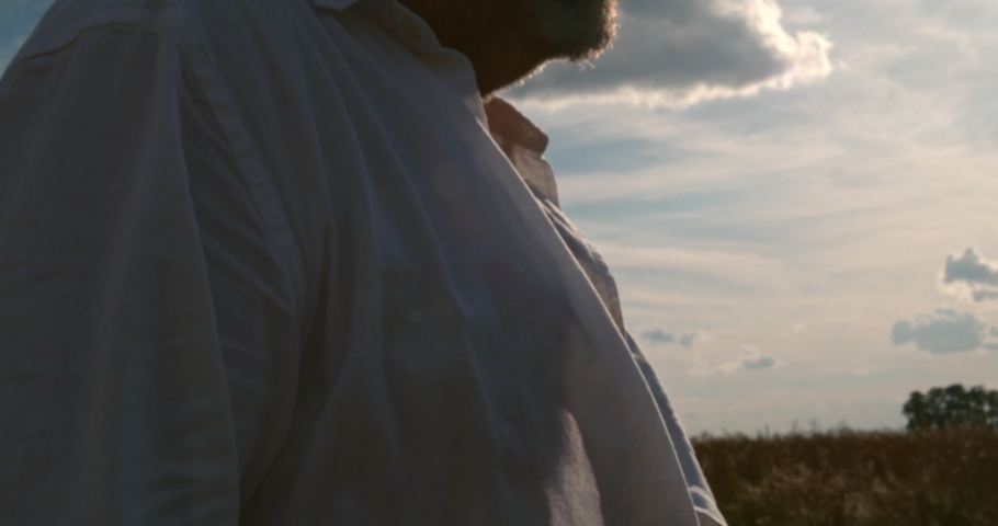 A man in a white shirt stands in the middle of the landscape. His white shirt flailing and flutters in the wind.
