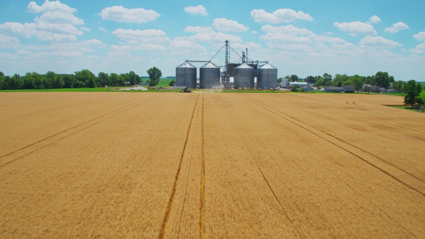 Rising drone shot over Ohio wheat field with combine harvester and grain elevator in the distance Royalty-Free Stock Footage #1092486461