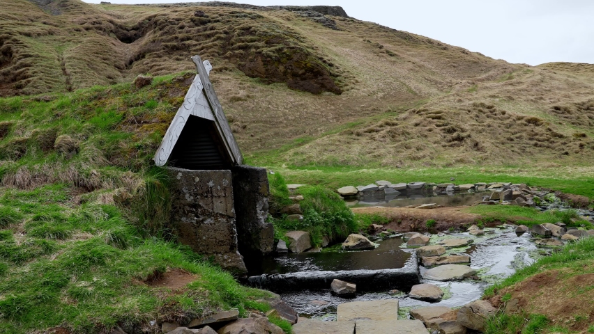 Beautiful geothermal hot spring and turf house in Hrunalaug in Iceland. Moss covered structure amidst rocks against mountain. Beautiful scenery of relaxing hot spring in Iceland.