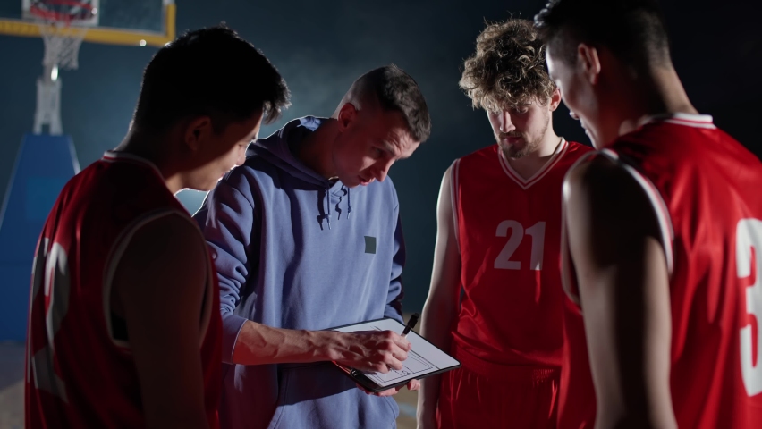 International basketball game, the coach instructs team players on the tactics of game, using a tablet and a marker for drawing, briefing before the game.